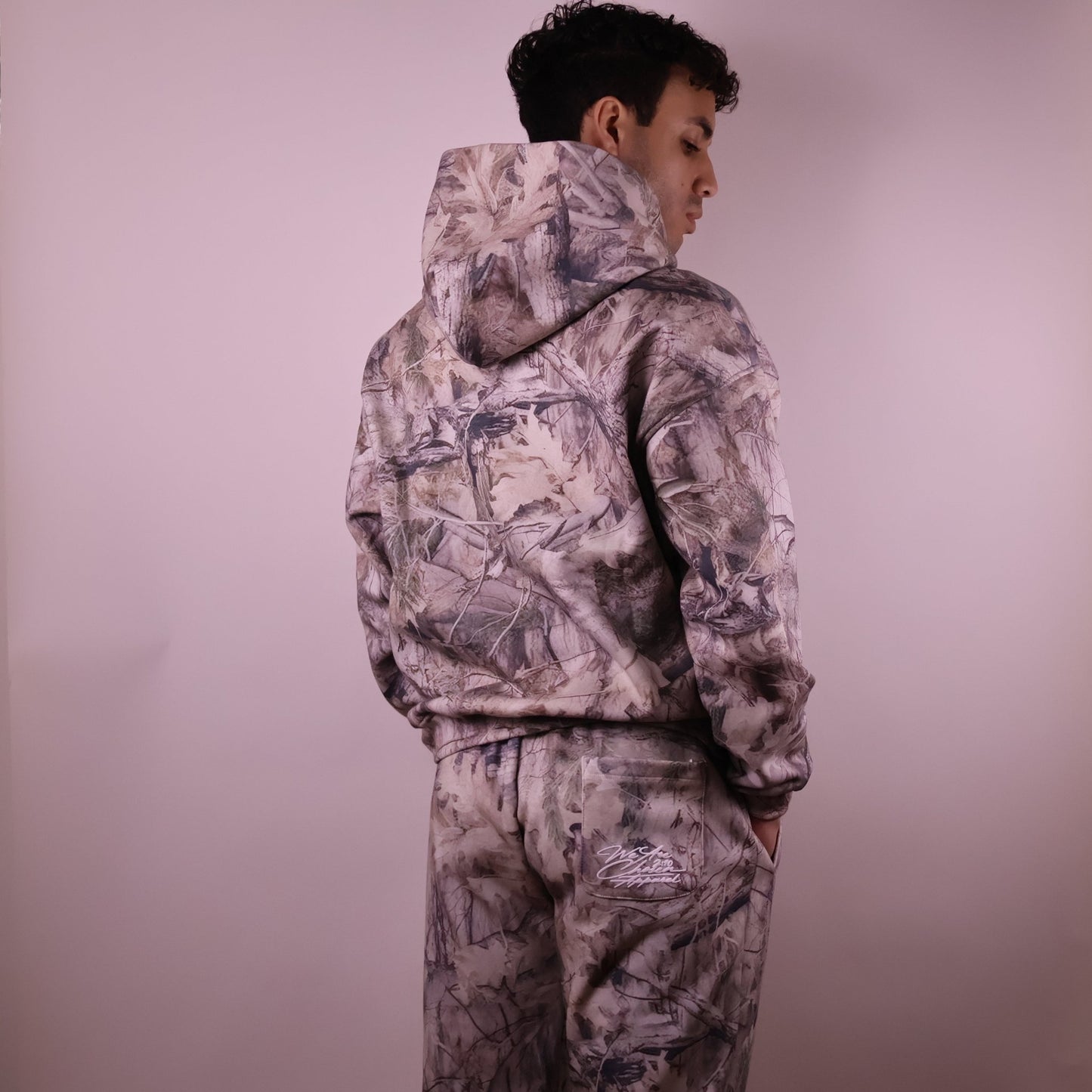 Person wearing a camouflage hoodie and pants against a plain background