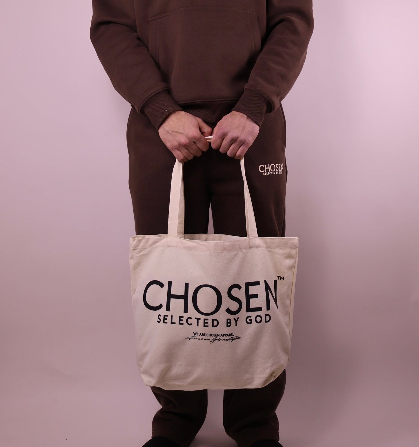 Person holding a tote bag with Chosen Selected by God text against a plain background