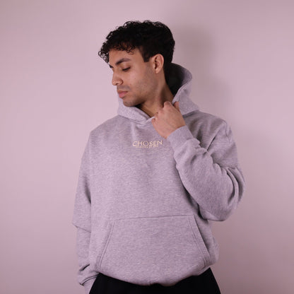 Man wearing a gray hoodie with Chosen branding against a light pink background