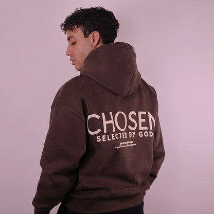 Man wearing a brown hoodie with Chosen Selected by God text on the back against a plain background