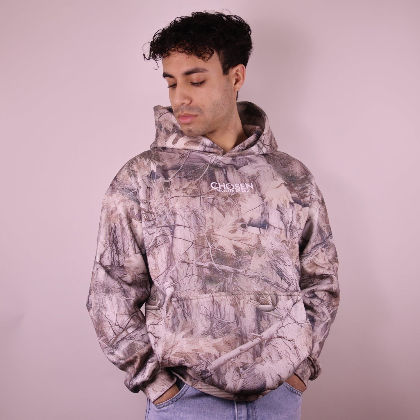 Person wearing a camouflage hoodie with a brand logo on a plain background