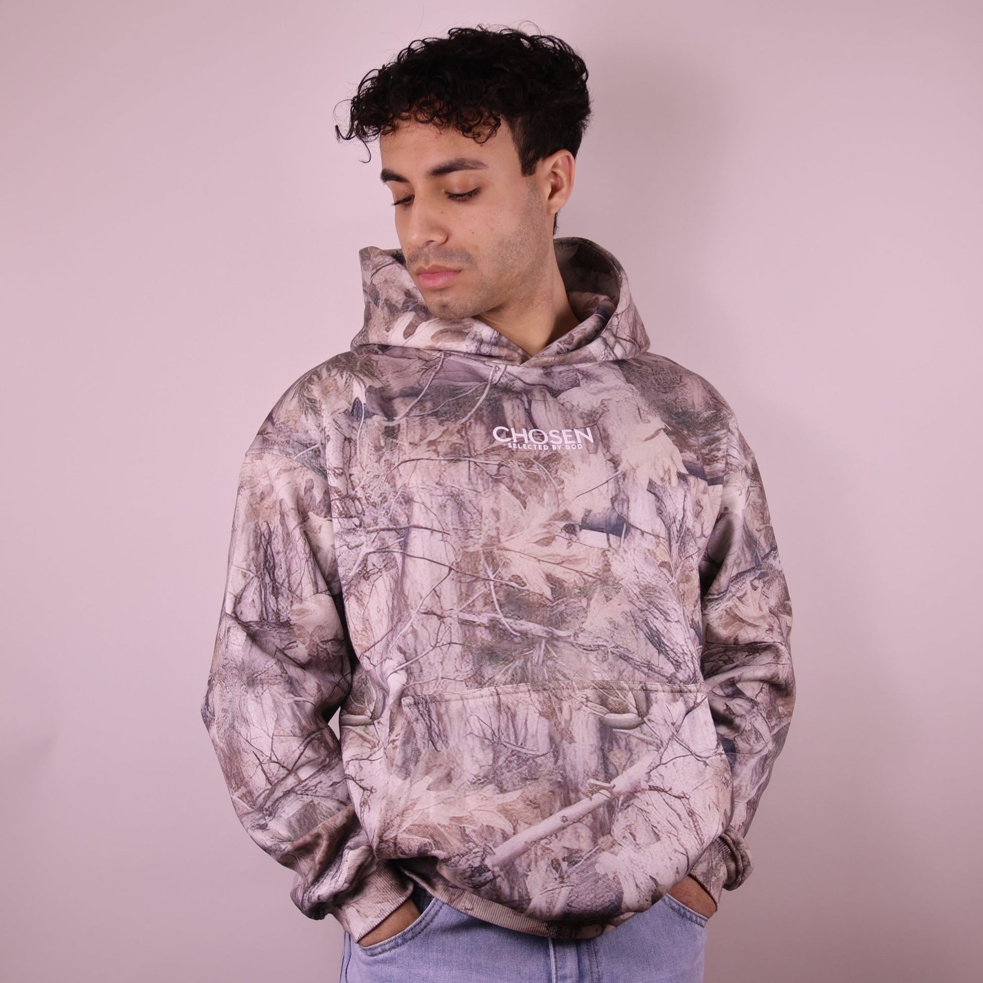 Person wearing a camouflage hoodie with a brand logo on a plain background