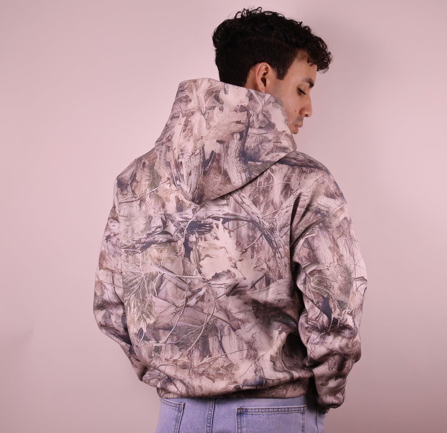 Person wearing a camouflage hoodie on a plain background