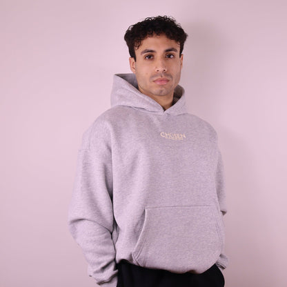 Man wearing a gray hoodie with a brand logo on a light pink background