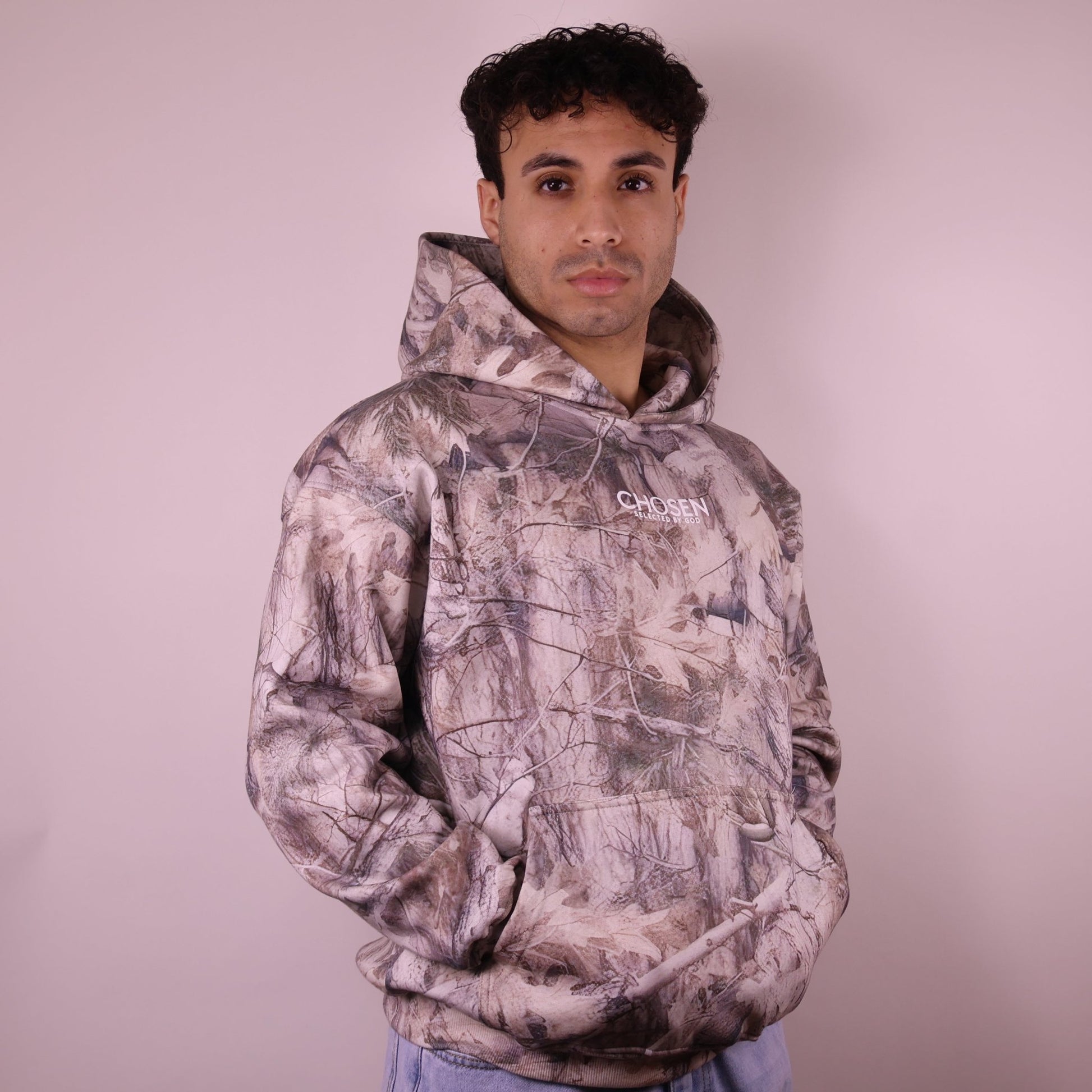Man wearing a camouflage hoodie with Chosen branding on a plain background