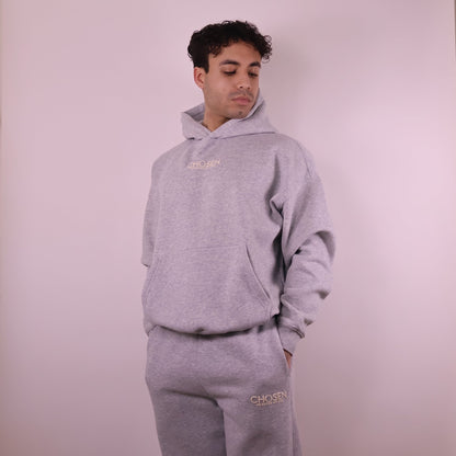 Person wearing a gray hoodie and pants with Chosen branding on a light pink background