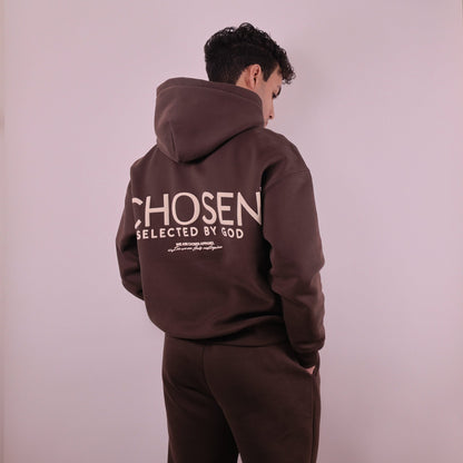 Person wearing a brown hoodie with Chosen Selected by God text on the back against a plain background