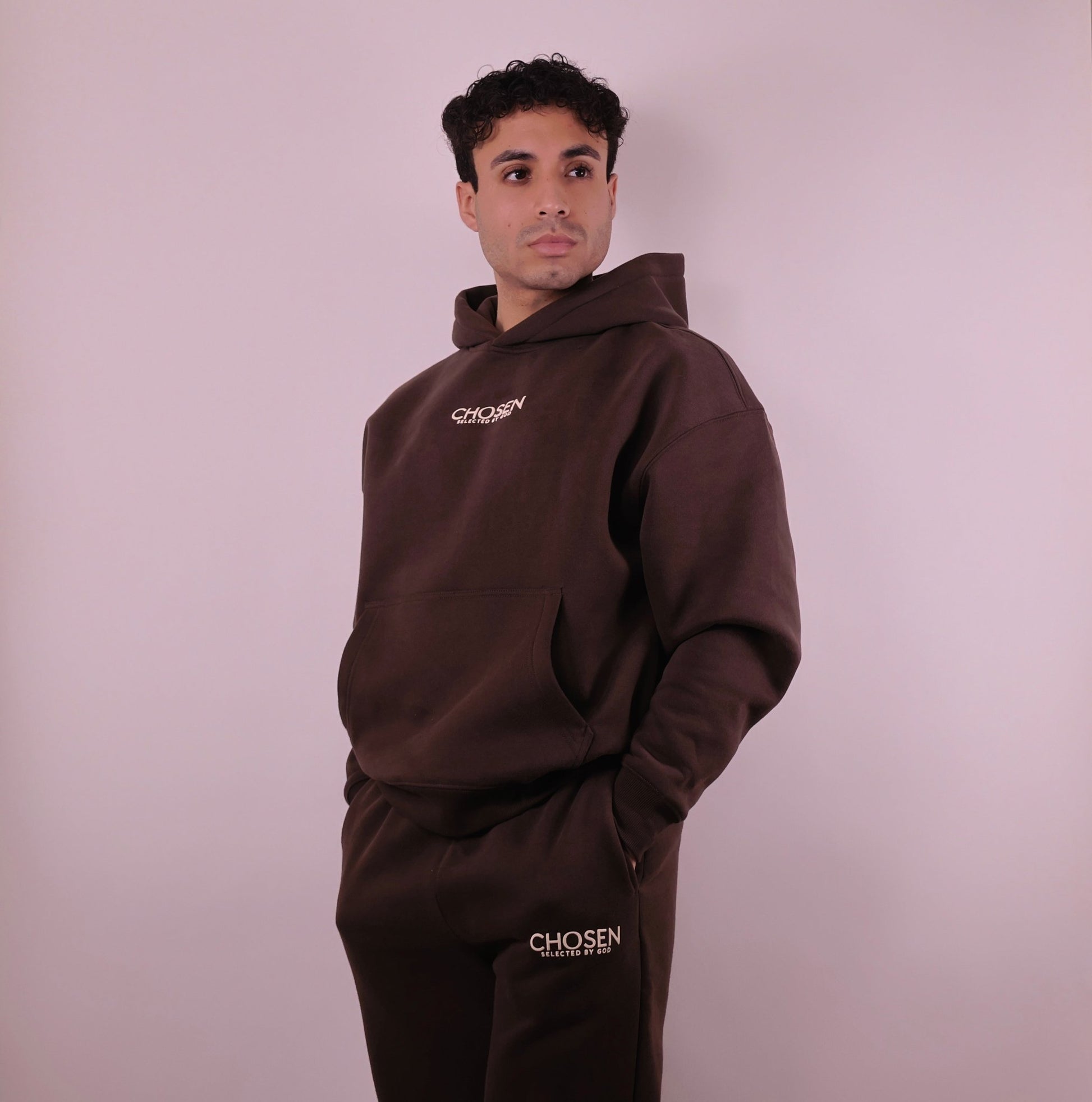 Man wearing a brown hoodie and pants with Chosen branding on a plain background
