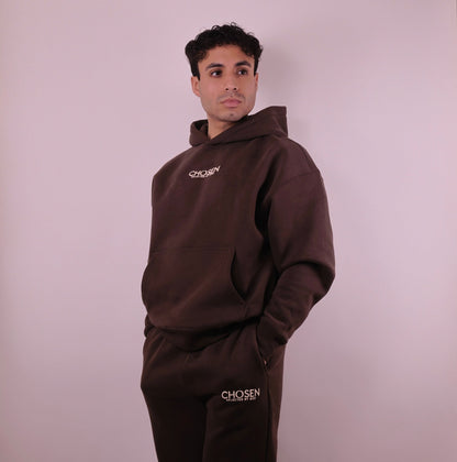 Man wearing a brown hoodie and pants with Chosen branding on a plain background