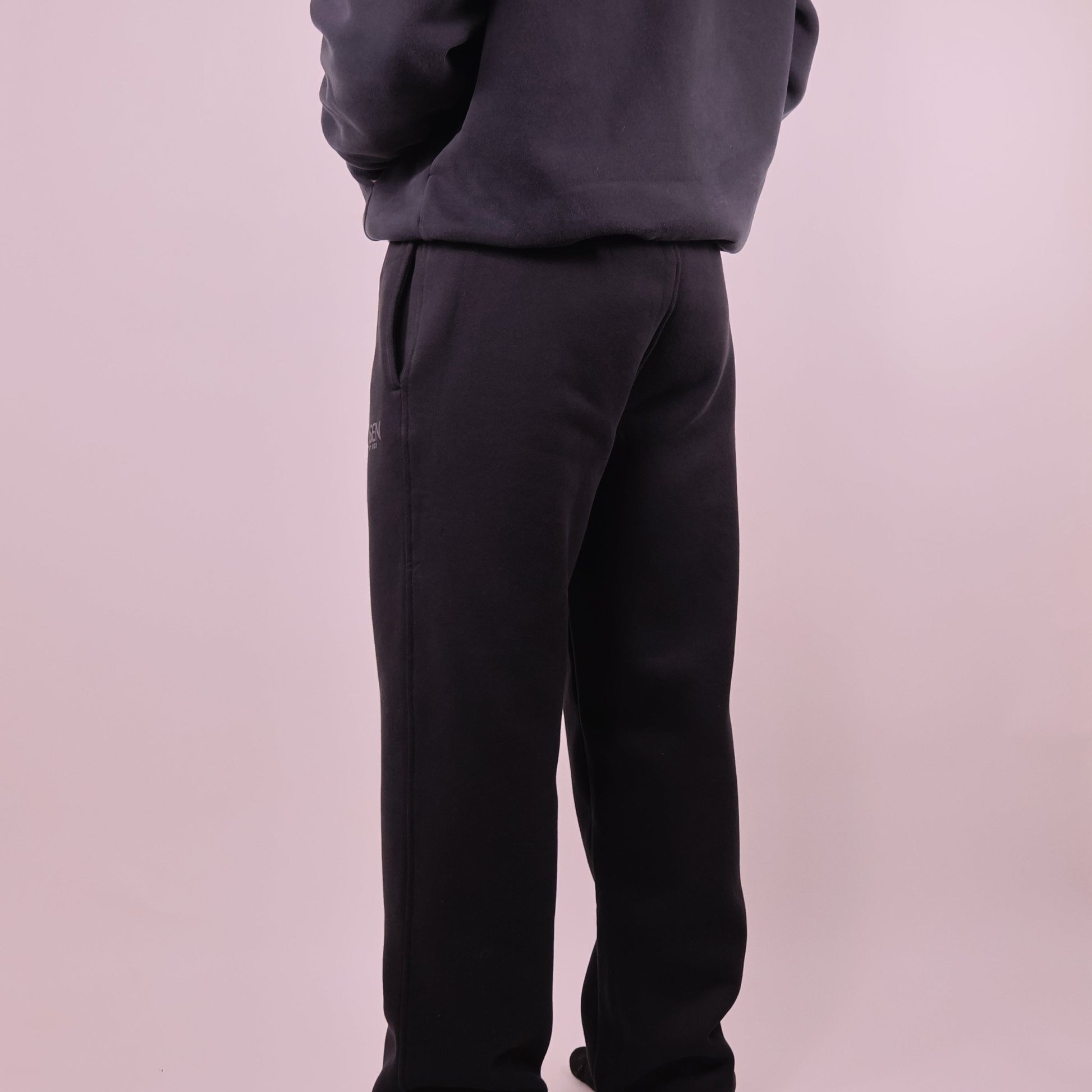Person wearing black pants and a dark jacket on a light pink background