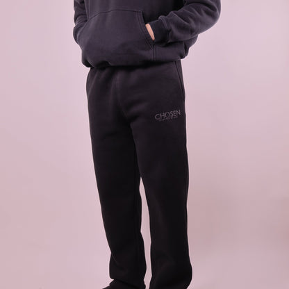 Person wearing black sweatpants with Chosen branding on a light pink background