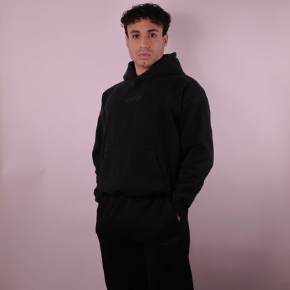 Man wearing a black hoodie and pants against a plain background