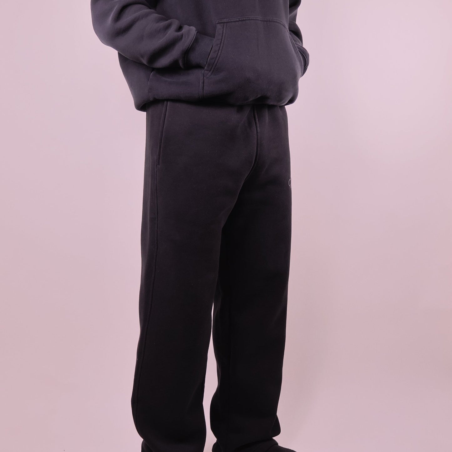 Person wearing black pants and a dark hoodie on a light pink background