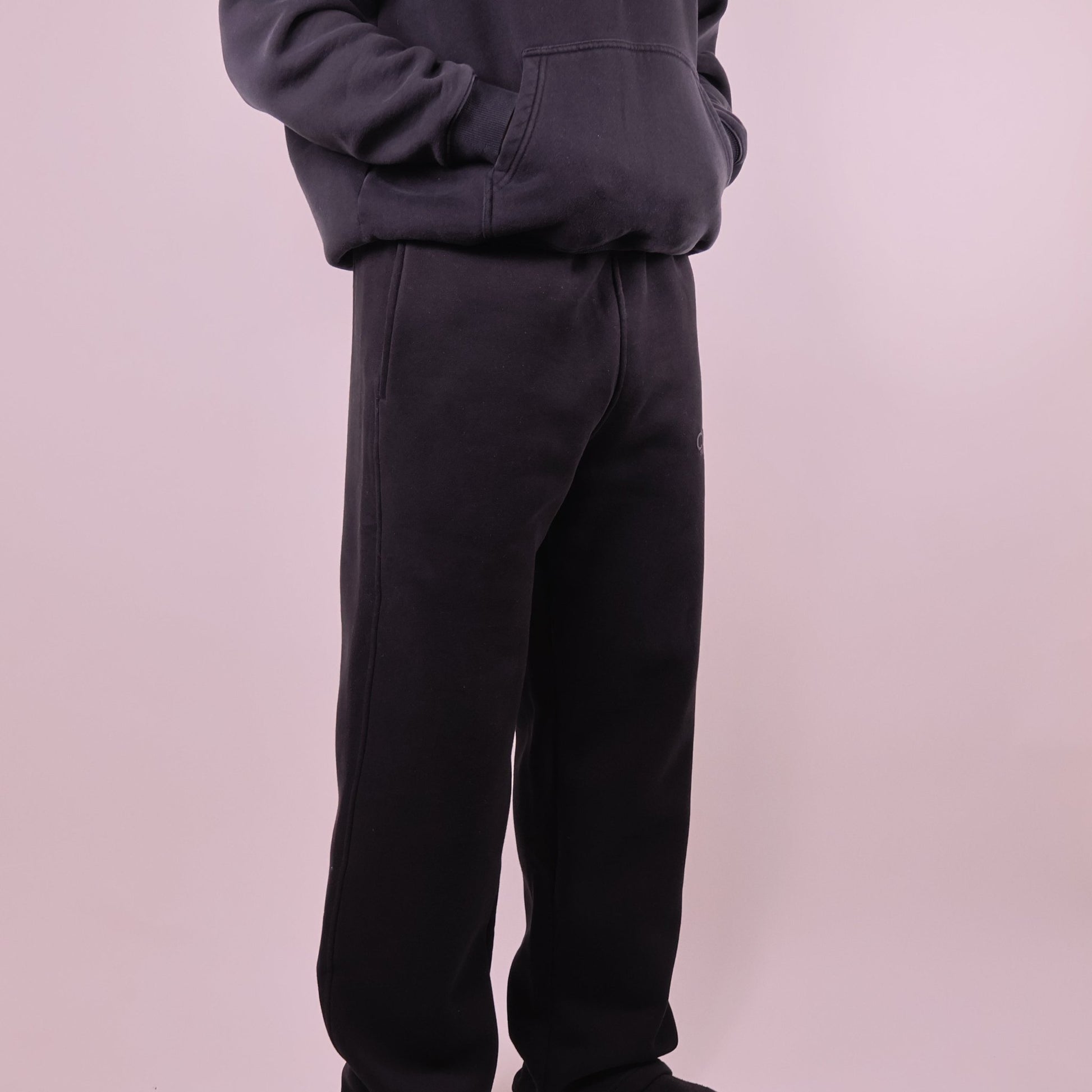 Person wearing black pants and a dark hoodie on a light pink background